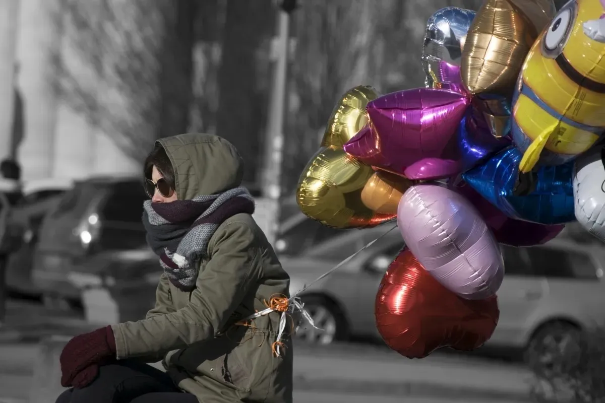 Person with balloons walking along a grayscale street